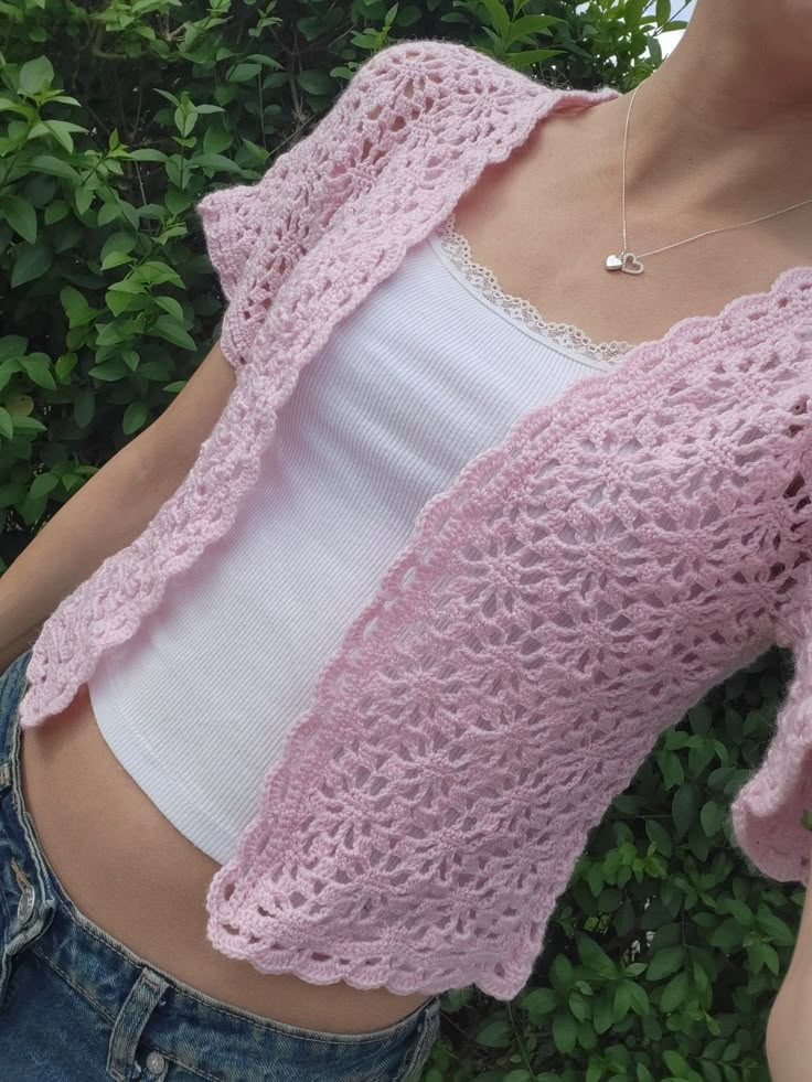 a woman is wearing a pink crochet shrugr over her top and jeans