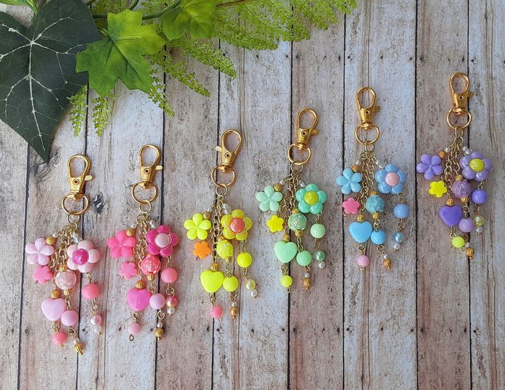 six key chains with different colored beads and charms hanging from them on a wooden surface