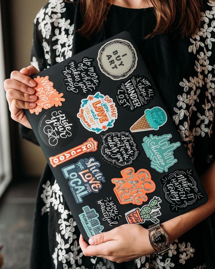 a woman is holding a black bag with various stickers on it