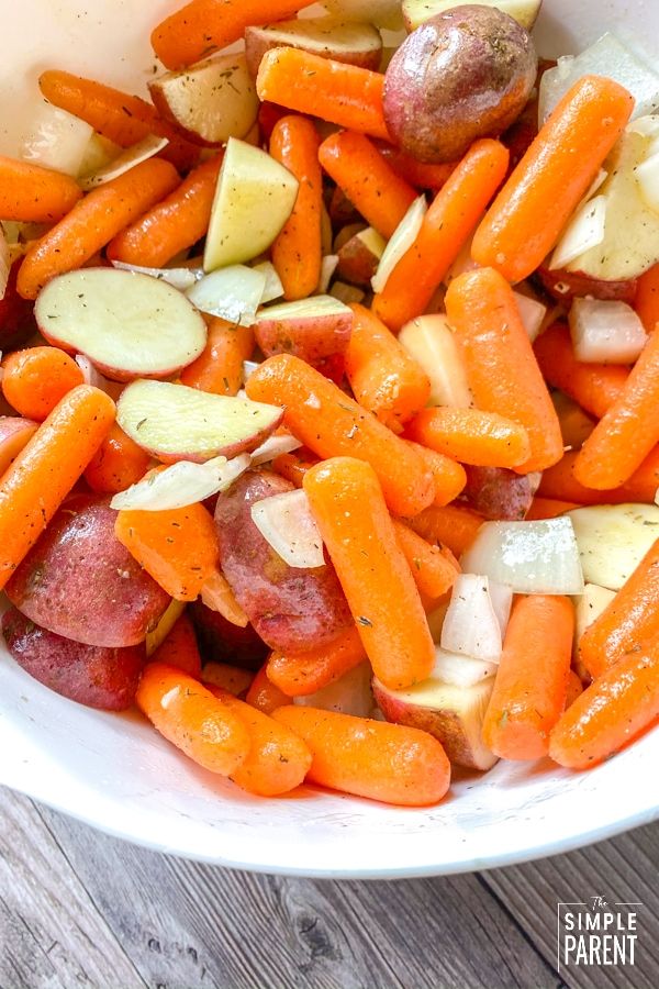 a bowl filled with carrots and potatoes on top of a wooden table