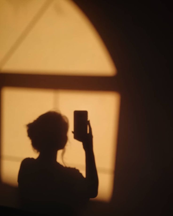 a woman holding up a cell phone in front of a window with the sun shining through it