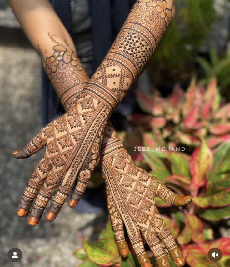 two hands with henna designs on them and some plants in the backgroud