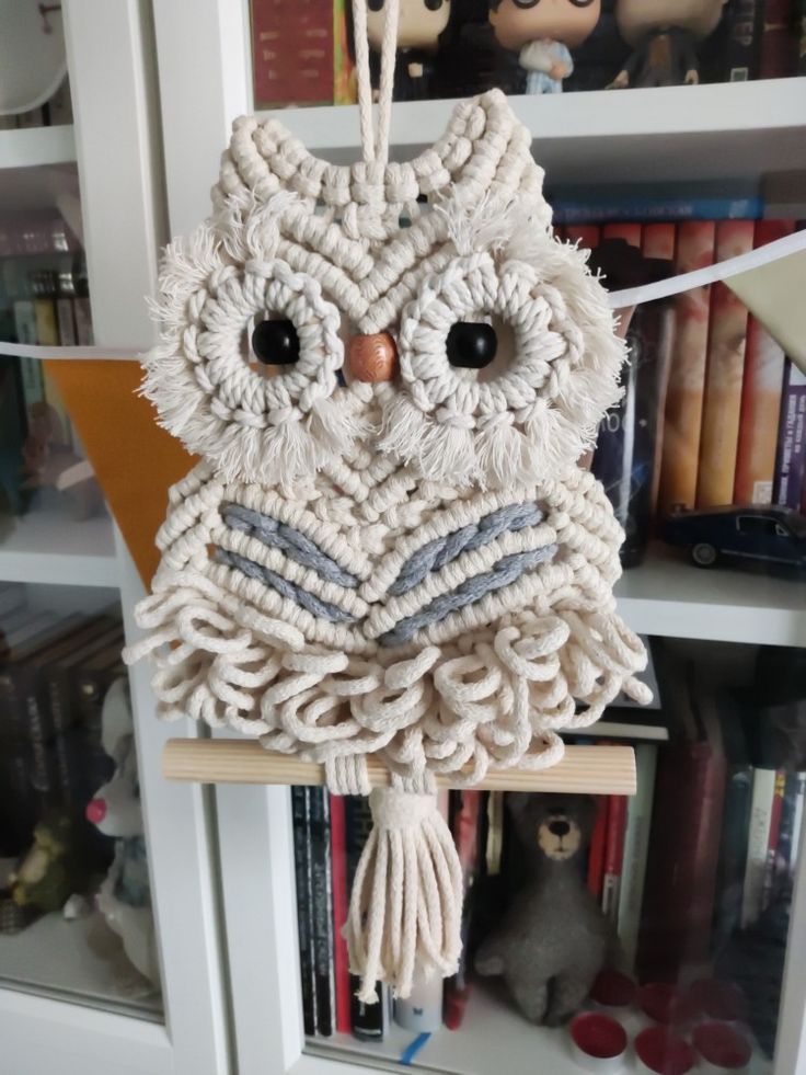 an owl made out of yarn hanging from a book shelf