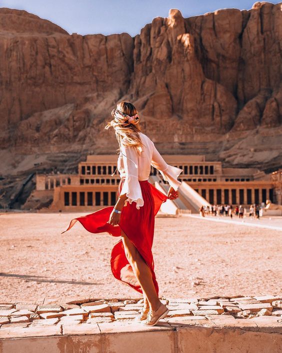 a woman in a red skirt and white shirt is walking across the desert