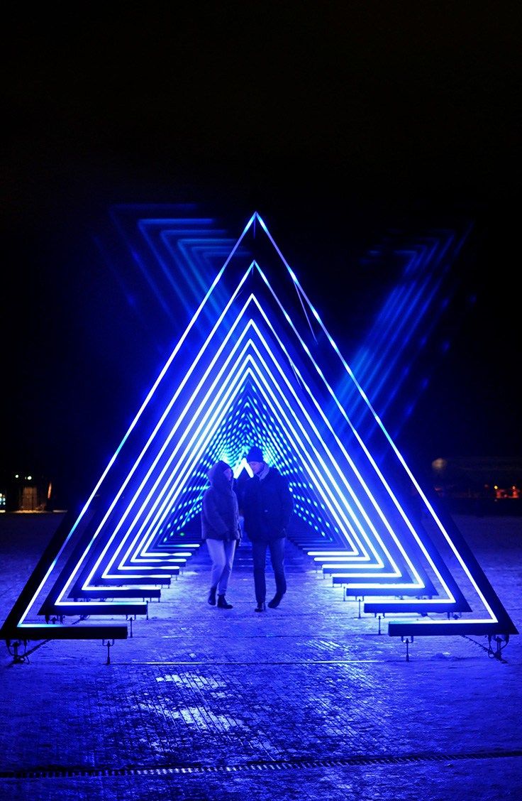 two people are standing in the middle of a blue light tunnel that is lit up at night