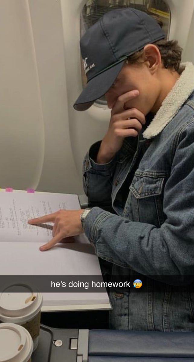 a man sitting on an airplane reading a book and pointing to the paper he's doing homework