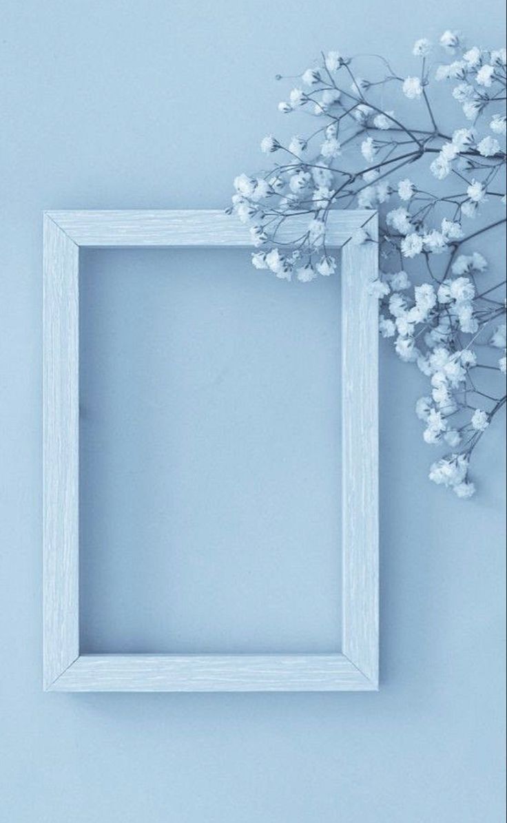 an empty white frame next to a bunch of baby's breath flowers on a blue background