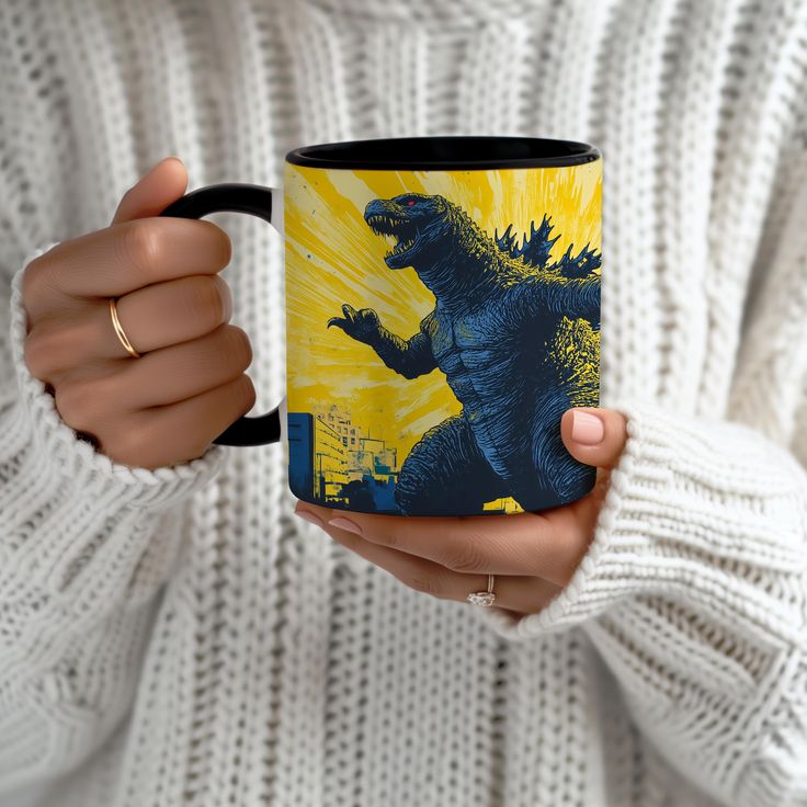 a woman holding a coffee mug with godzilla on the front and yellow background in her hands