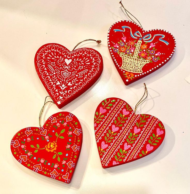 four heart shaped ornaments hanging from strings on a white surface with red and pink designs