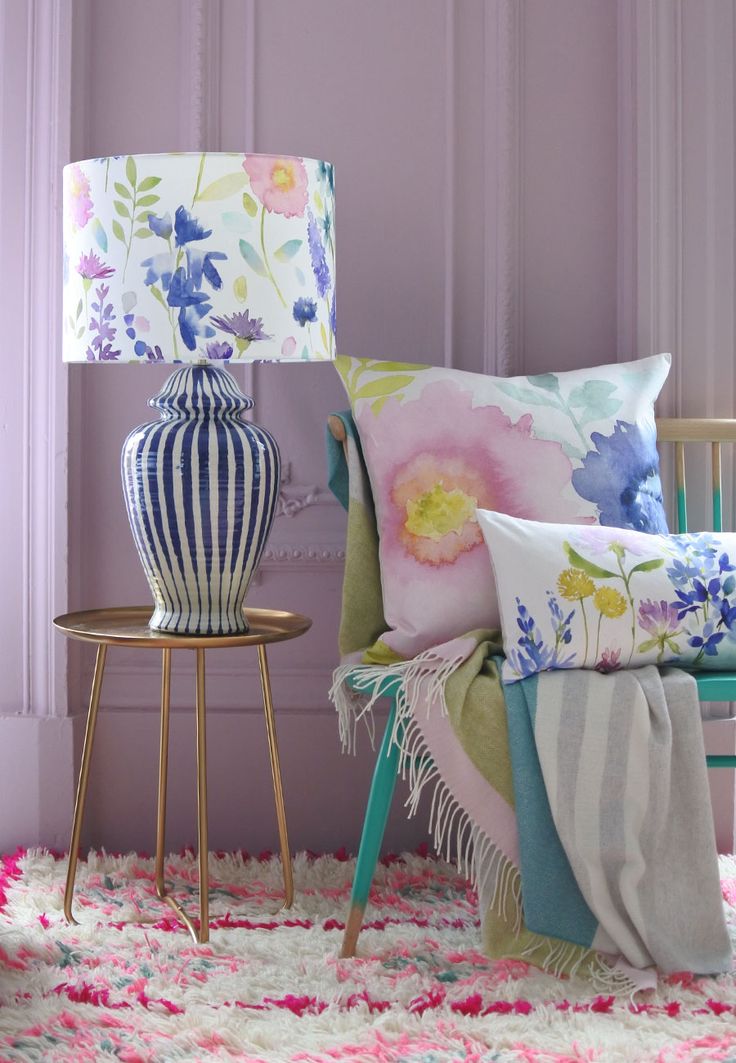 a chair with pillows and a lamp on top of it next to a rug in front of a purple wall