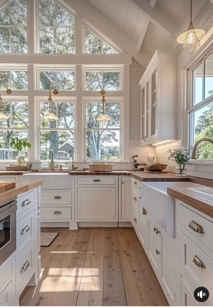 a large kitchen with white cabinets and wood flooring is pictured in this image, there are two windows above the sink