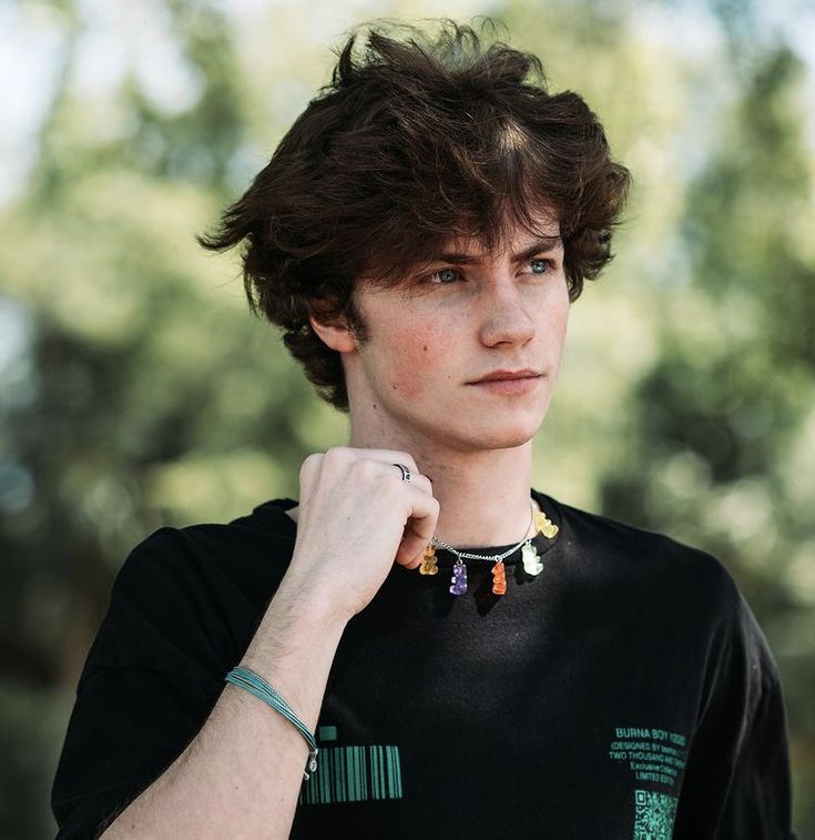 a young man wearing a black t - shirt is posing with his hand on his shoulder