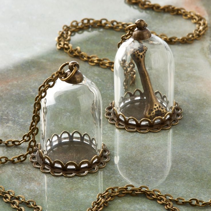 two glass bell jars sitting on top of a table next to a gold chain necklace