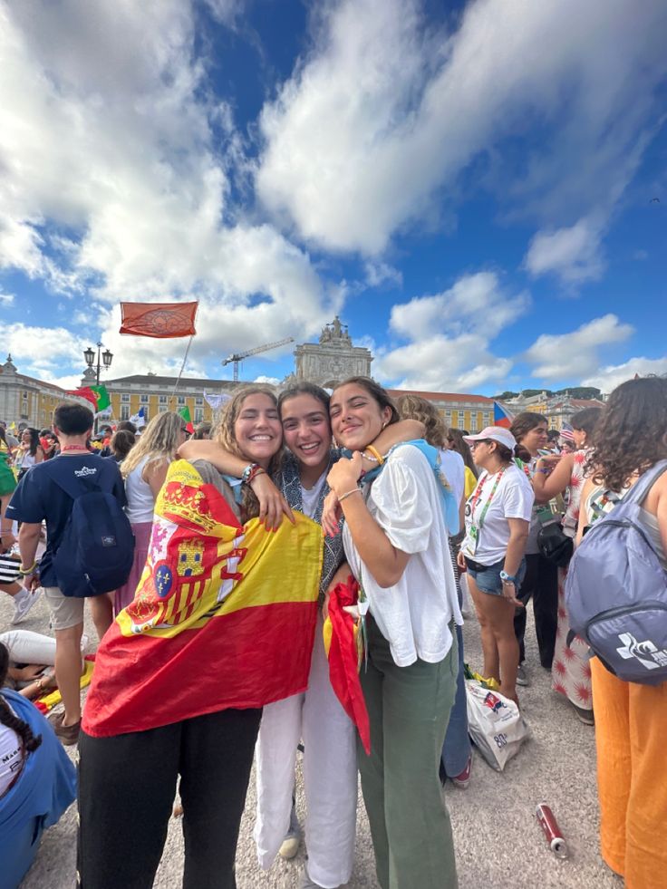 two young women hugging each other in front of a large group of people on a sunny day