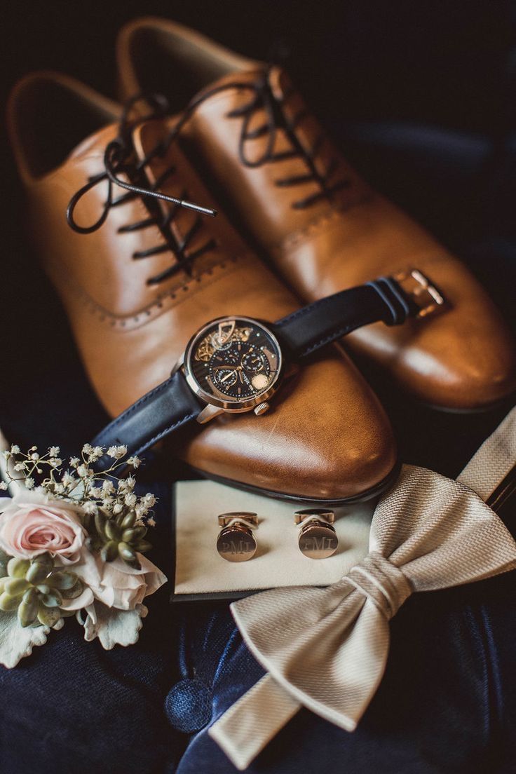 a pair of brown shoes sitting on top of a pile of clothing and flowers next to a watch