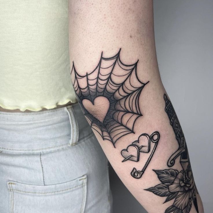 a woman's arm with a spider web tattoo on it and a heart in the center