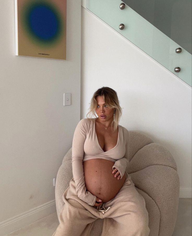 a pregnant woman sitting on a bean bag chair in front of a stair case and painting