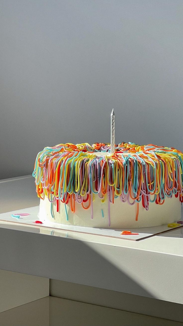 a birthday cake decorated with multicolored icing and a single candle on top