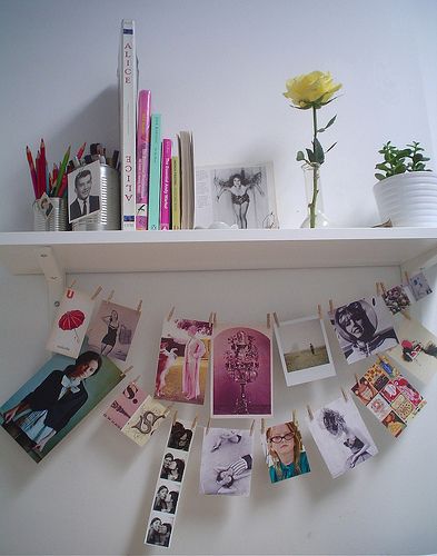 several pictures are hanging on the wall with clothes pins attached to them, and there is a yellow flower next to it