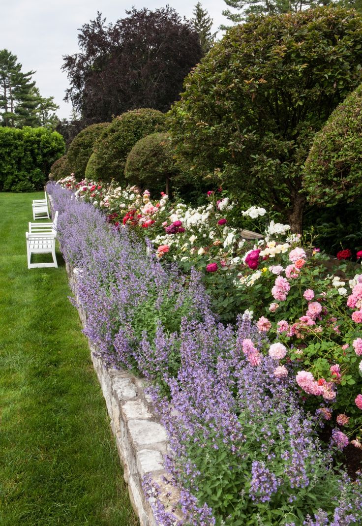 a garden filled with lots of flowers next to a white bench on top of a lush green field