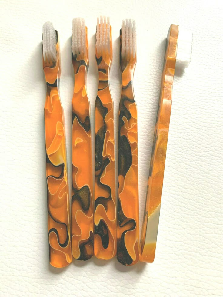 three toothbrushes with orange and black designs sitting next to each other on a white surface