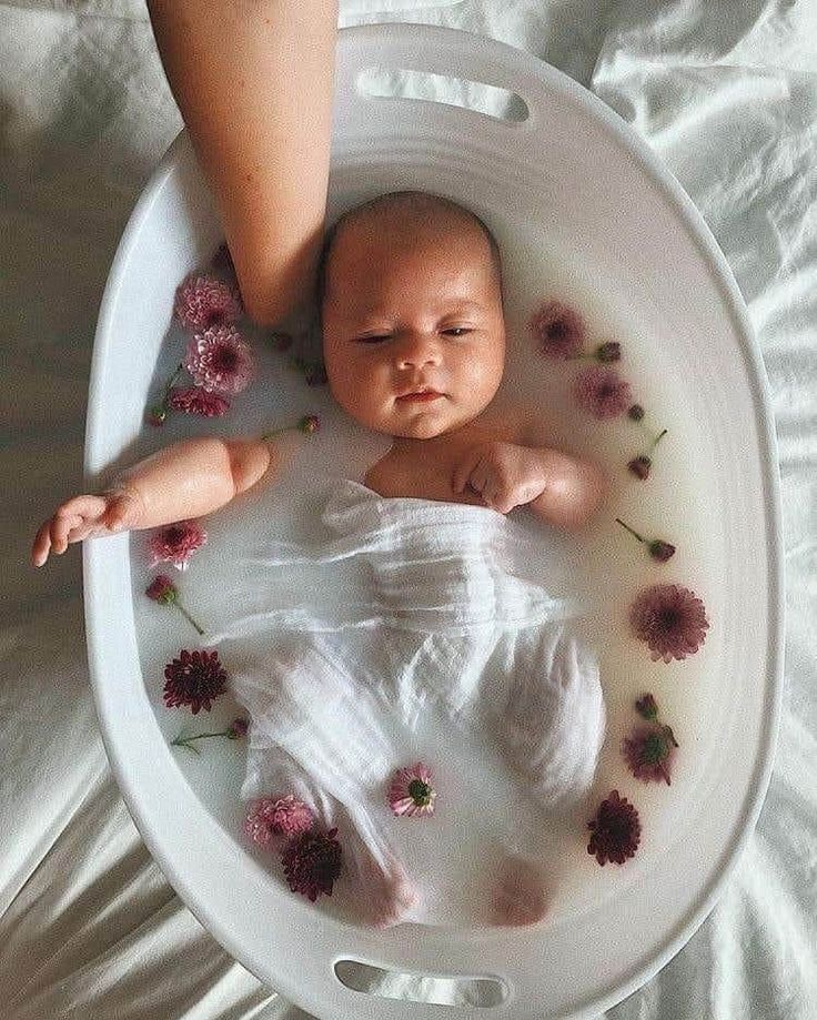 a baby laying in a bathtub with flowers on the floor next to someone's foot