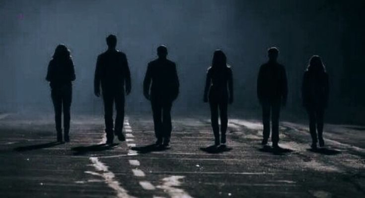 the silhouettes of five people standing in an empty parking lot at night, with one person looking on