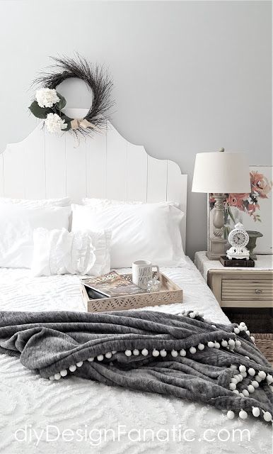 a white bed topped with pillows and blankets next to a wreath on the headboard