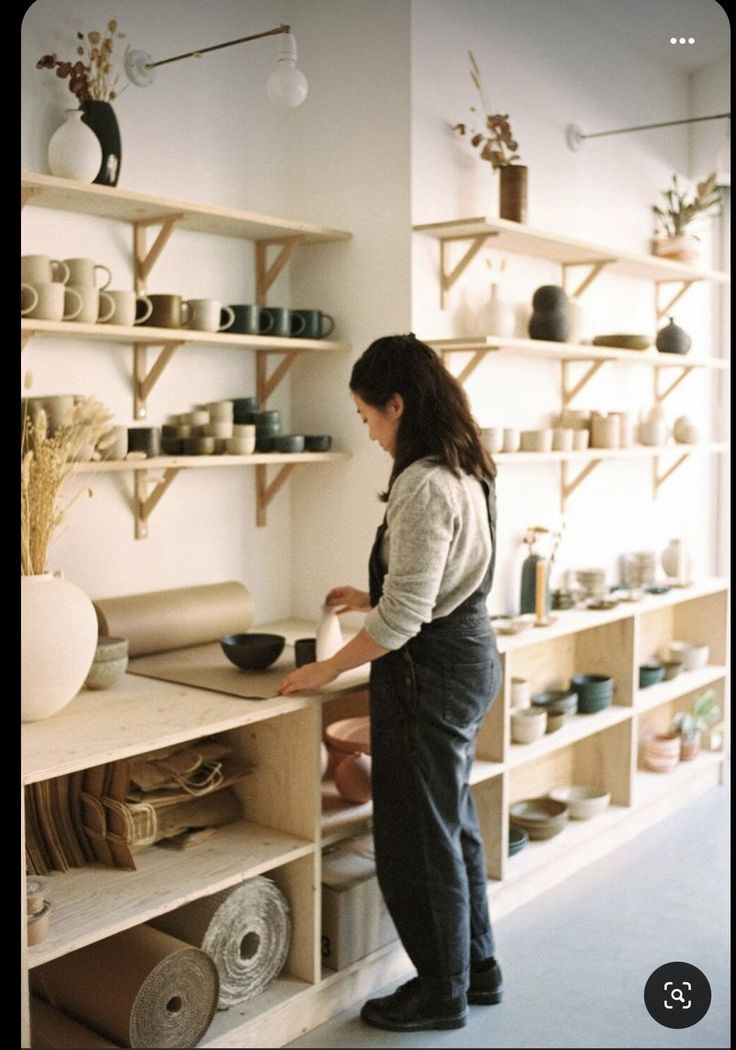 a woman standing in front of a shelf filled with pots and bowls