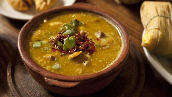 a brown bowl filled with soup on top of a wooden table next to some bread