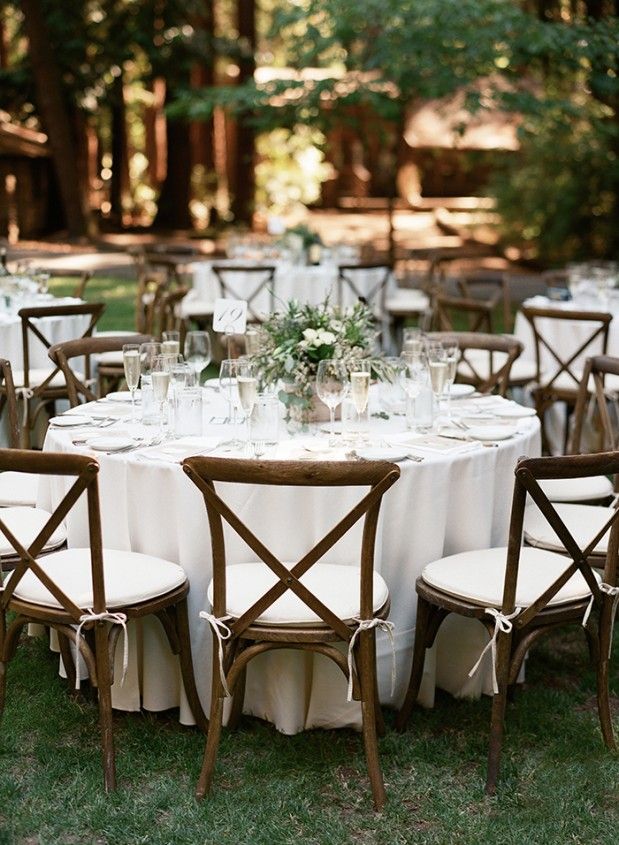 a table set up with white linens and wooden chairs for an outdoor wedding reception