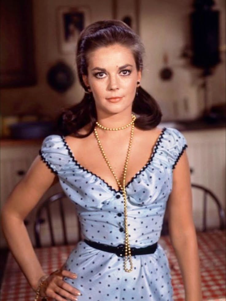 a woman in a blue dress standing with her hands on her hips and looking at the camera