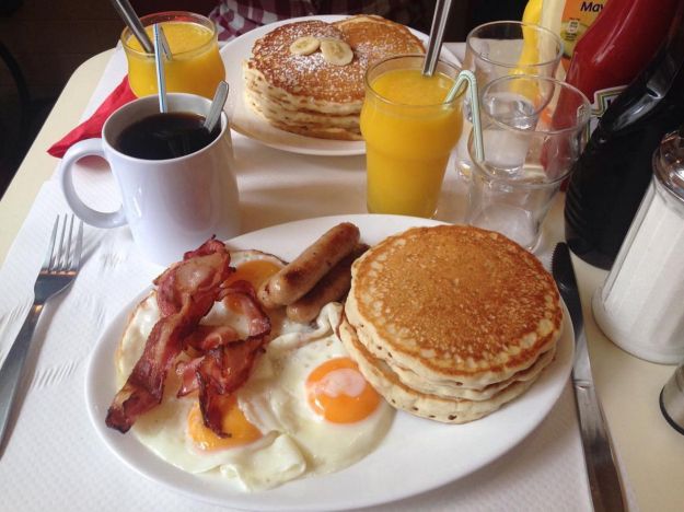 a breakfast plate with pancakes, bacon and eggs