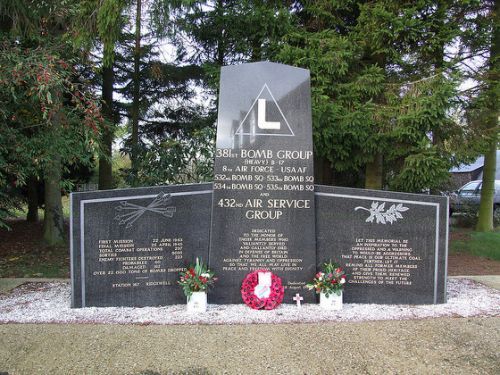 a memorial with flowers and wreaths on the ground in front of it, surrounded by trees