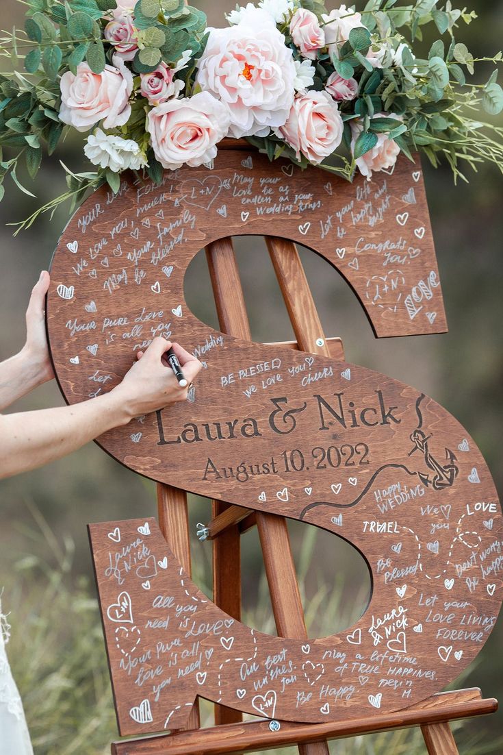 a wooden sign with writing on it and flowers in the top, is being held up by a woman