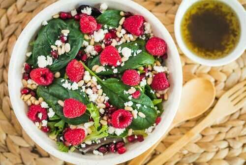 a white bowl filled with spinach and raspberries next to a cup of tea