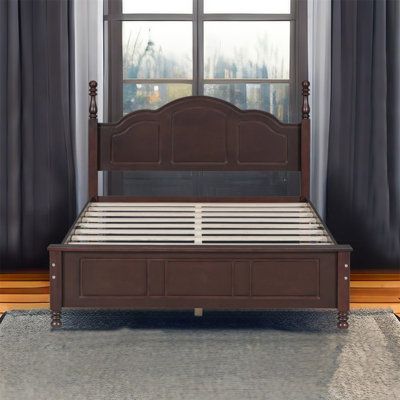 a bed sitting in front of a window next to a wooden frame and headboard