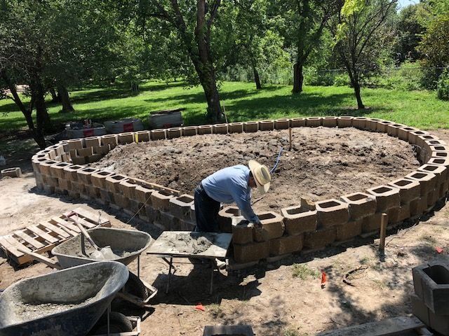 a man is building a brick wall in the middle of a yard with concrete blocks