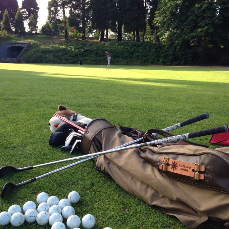 golf balls and clubs laying on the grass in front of a bag with two men's tees next to it