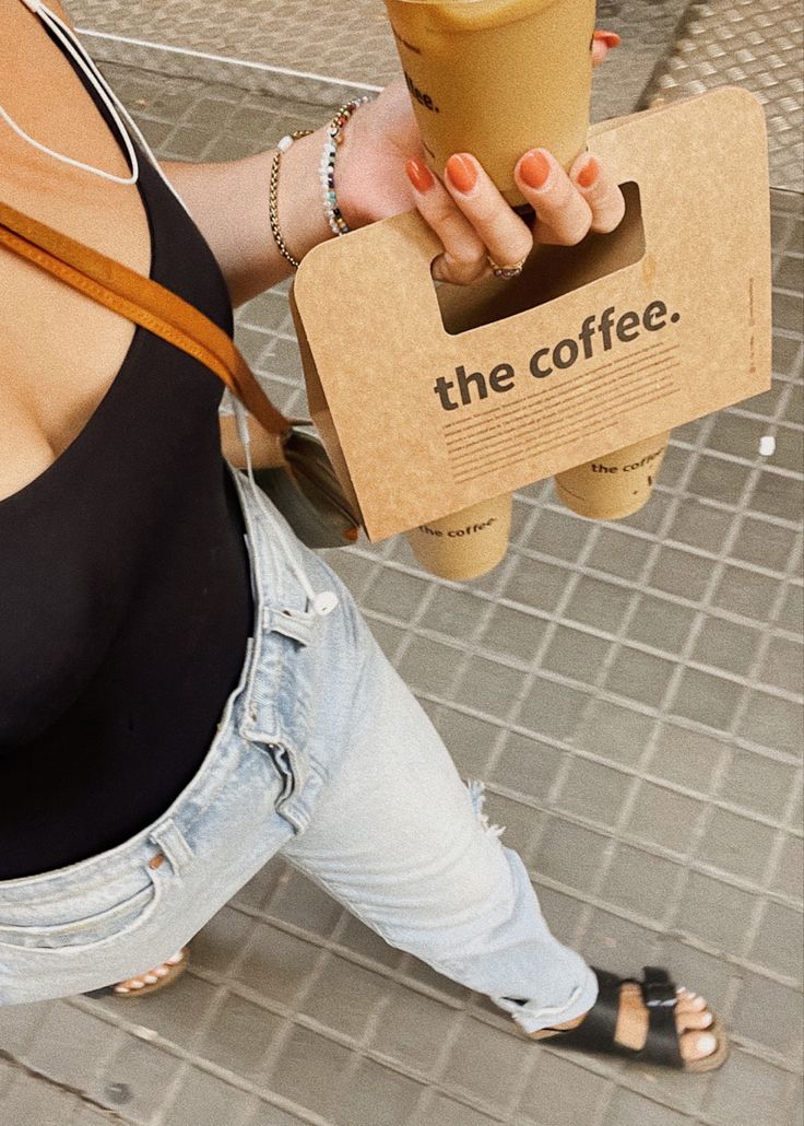 a woman holding up a box with a drink in it and the words the coffee on it