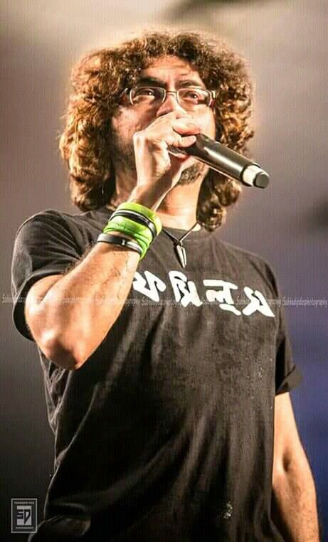 a man with long curly hair and glasses holding a microphone to his mouth while standing on stage