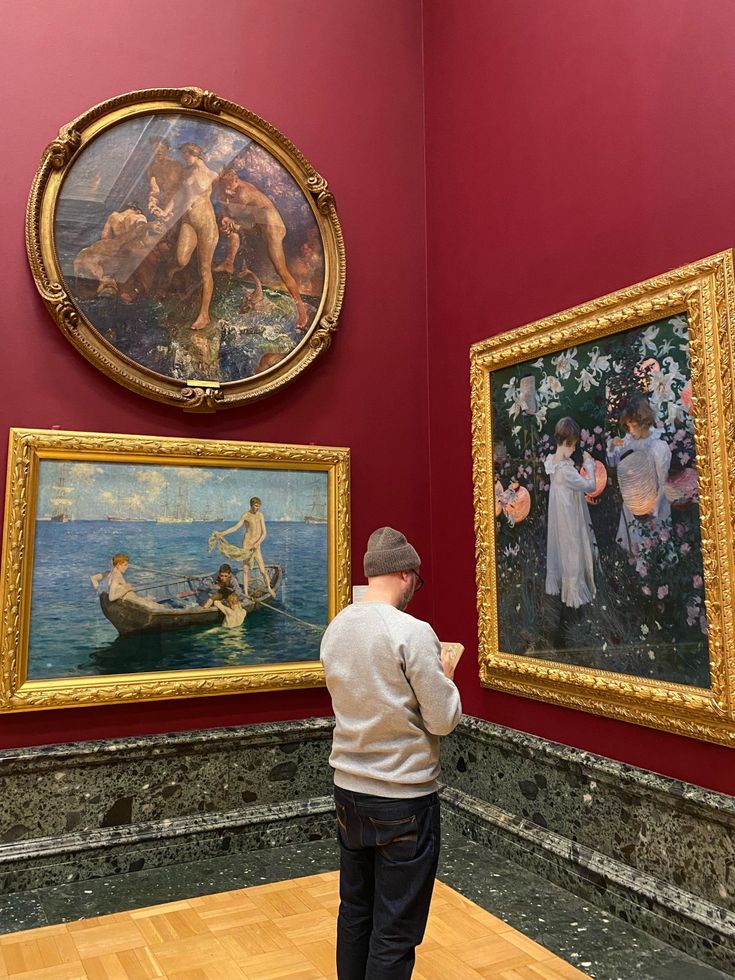 a man looking at paintings on display in a room with wooden floors and red walls