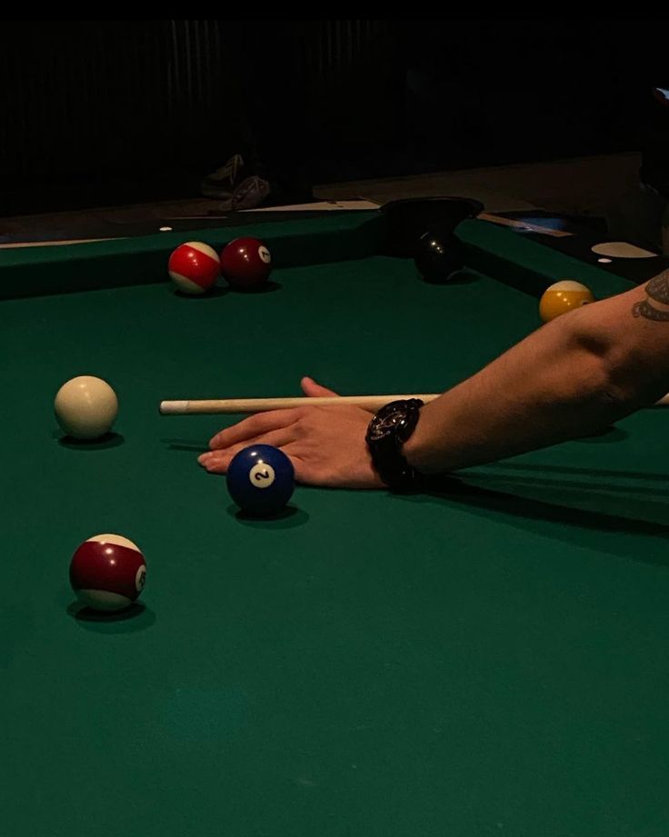 a man is playing pool with his hand on the ball and cues in front of him