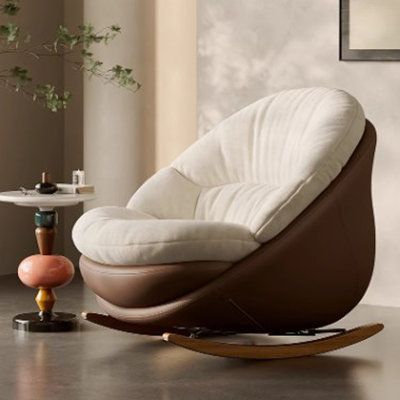 a white and brown chair sitting in a living room next to a table with a vase on it