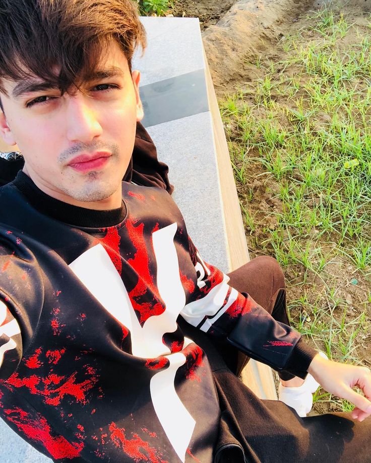 a young man sitting on top of a wooden bench next to a green grass covered field