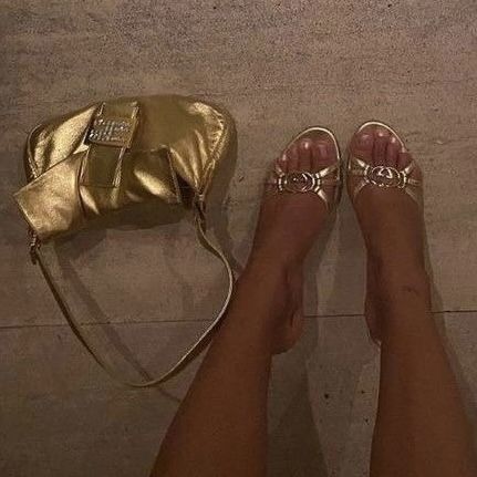 a woman's feet with gold shoes and a purse on the ground next to her