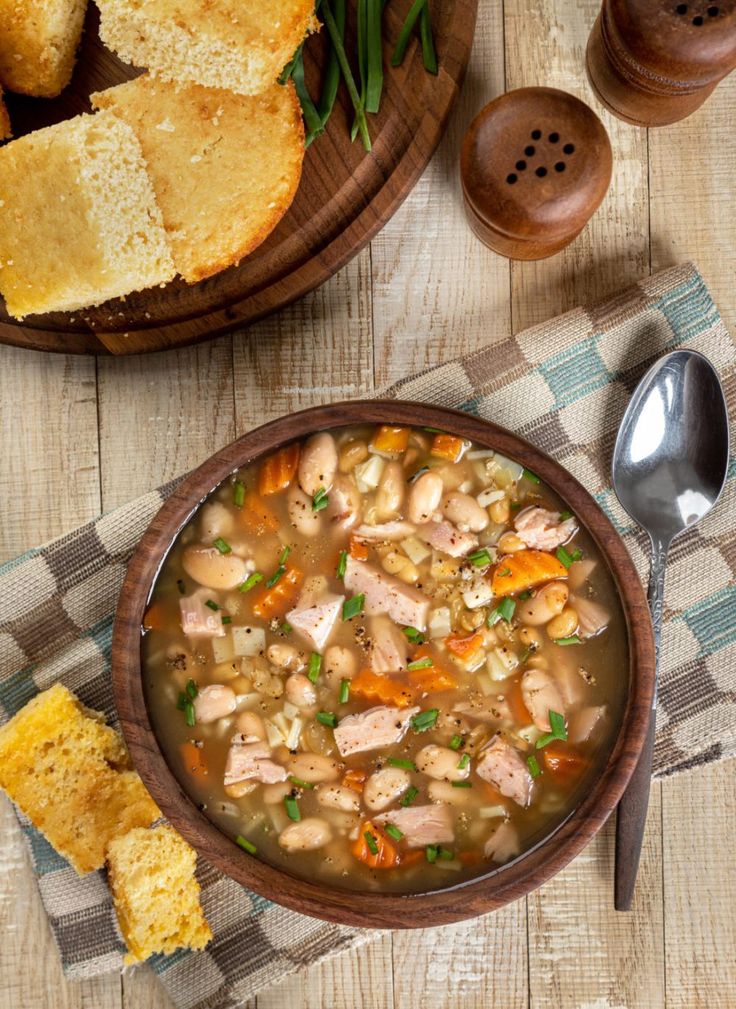 a bowl of chicken and bean soup next to bread on a checkered table cloth