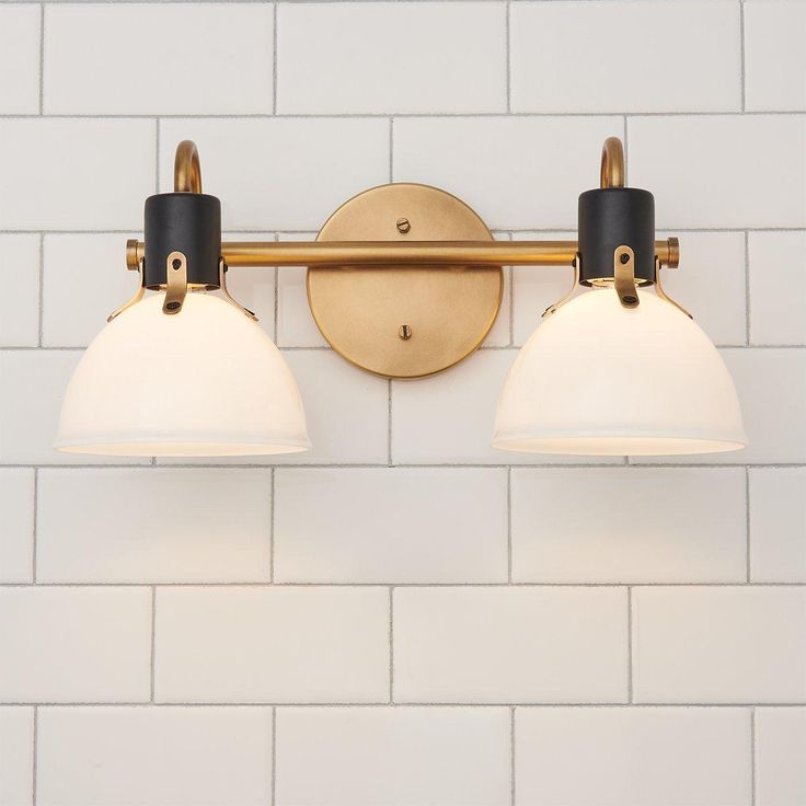 two light bathroom fixture with white and black shades on the wall above it, against a white tile background