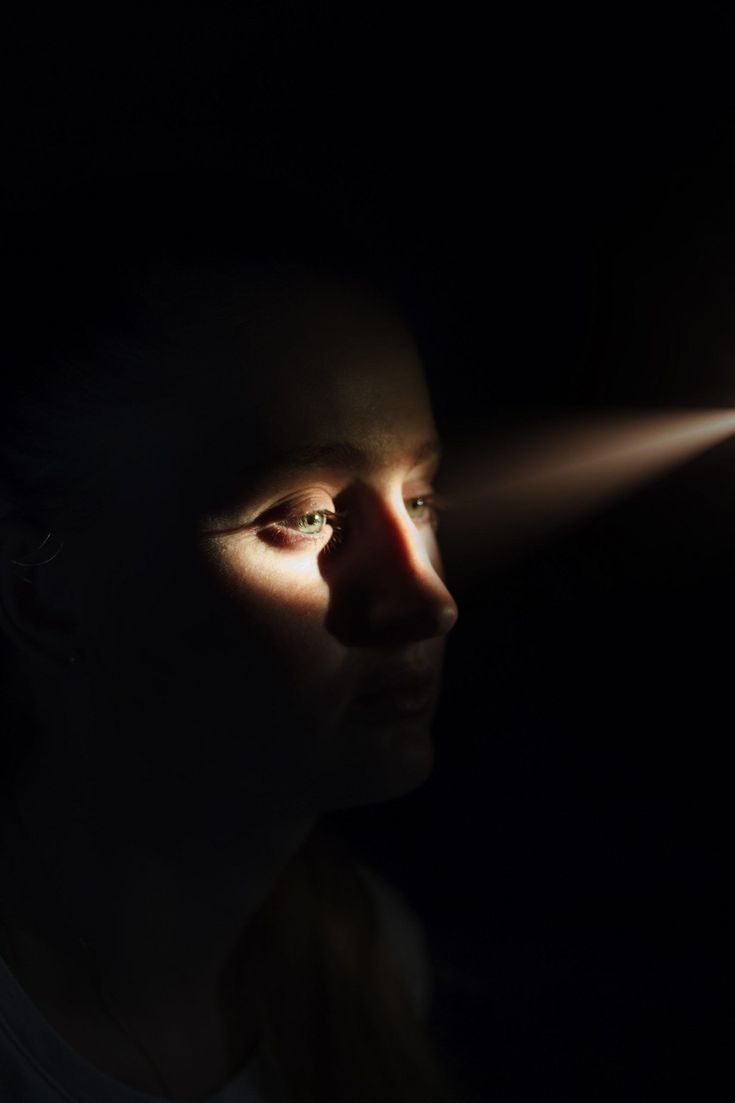 a woman in the dark looking at something with light coming from her face and arm