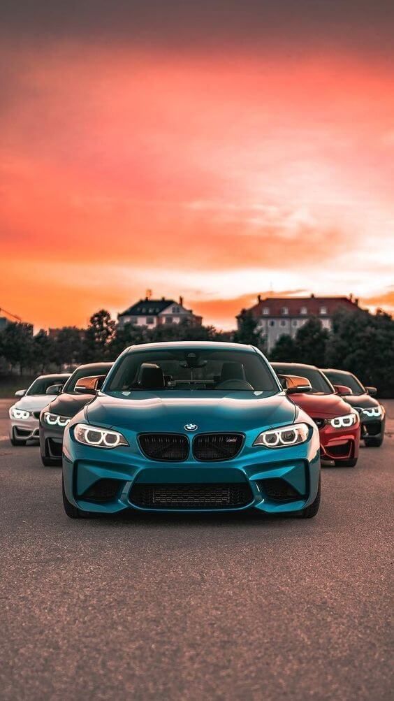 four bmw cars parked in a parking lot with the sun setting behind them and an orange sky